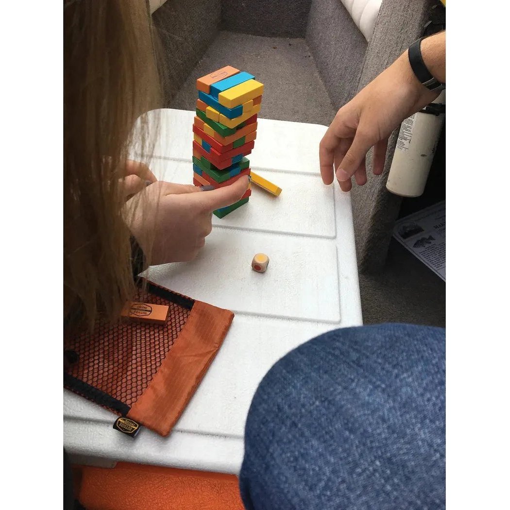 A person points at the GSI Outdoors Backpack Tumbling Tower on a white table with a small wooden block nearby.