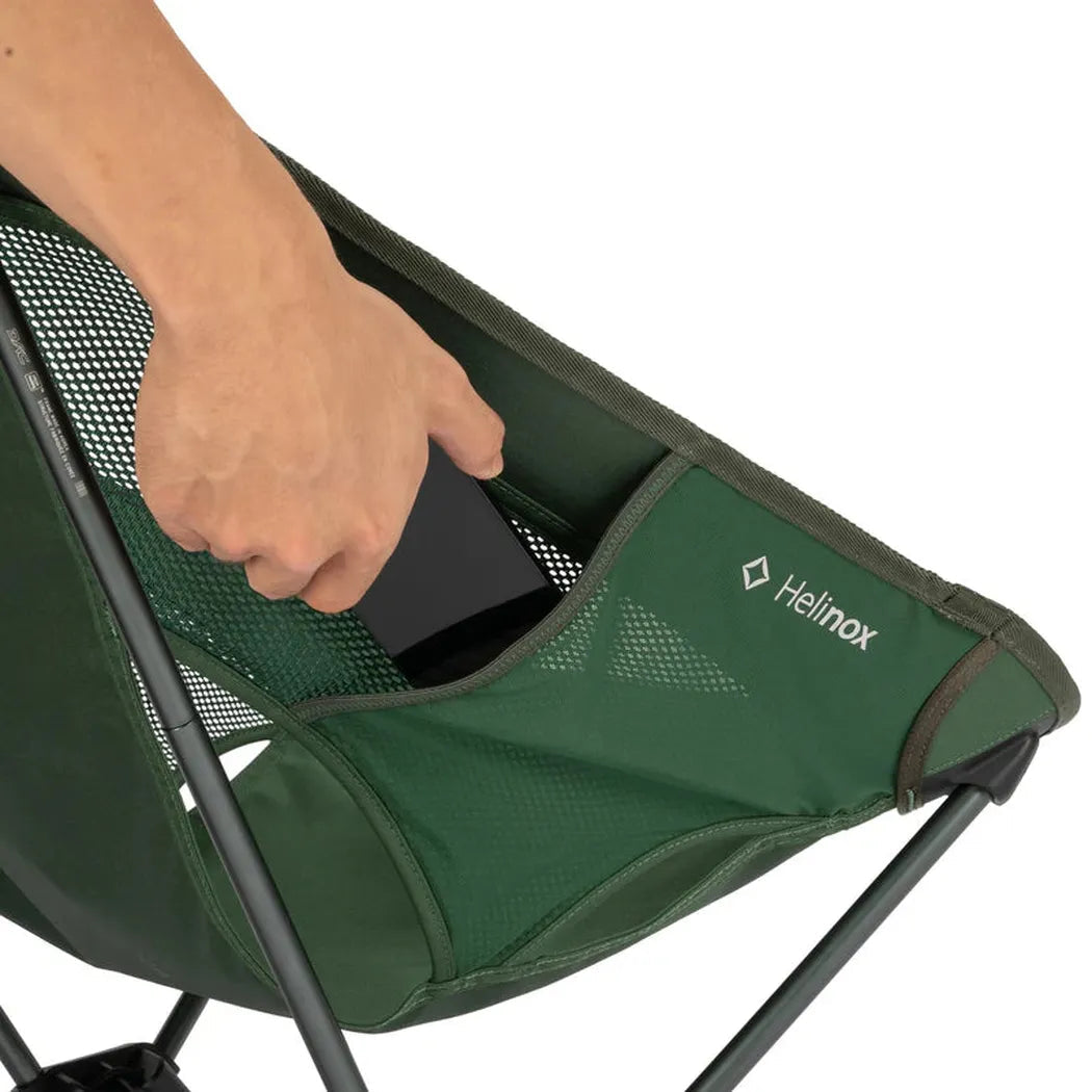 A hand puts a phone in the pocket of a green Helinox Chair One against a white background.