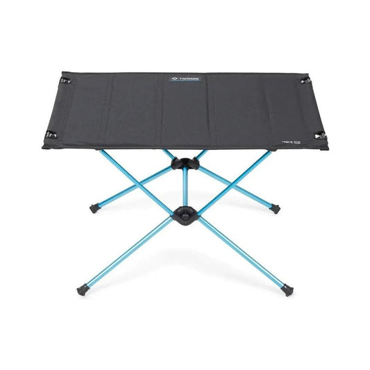 A top-down view of the Helinox Table One Hard Top in Black R1 with a blue metal frame and black rubber feet, set against a white background.