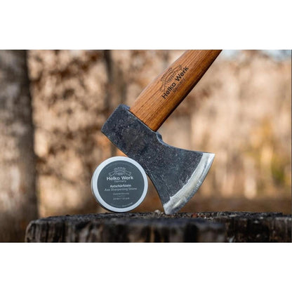 A Helko Werk Axe Sharpening Stone sits next to a Helko Werk axe on a tree stump with a forest background.