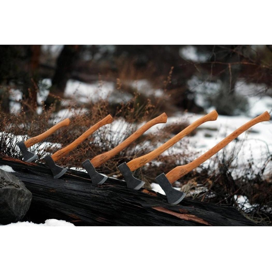 Five Helko Werk Bavarian Woodworker axes with wooden handles rest on a log in a snowy, wooded outdoor setting.