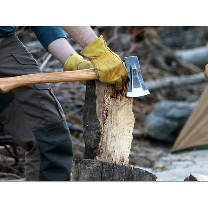 A person wearing yellow gloves holds the Helko Werk Heidelberg Mini Spalter axe on a log, with a tent and logs in the background.