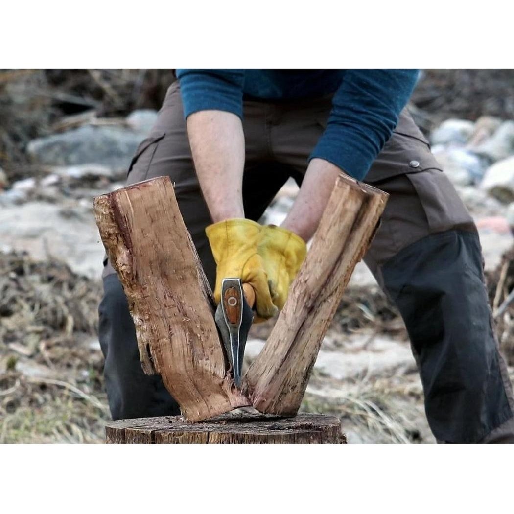 A person wearing yellow gloves splits wood with the Helko Werk Heidelberg Mini Spalter on a tree stump in an outdoor setting.