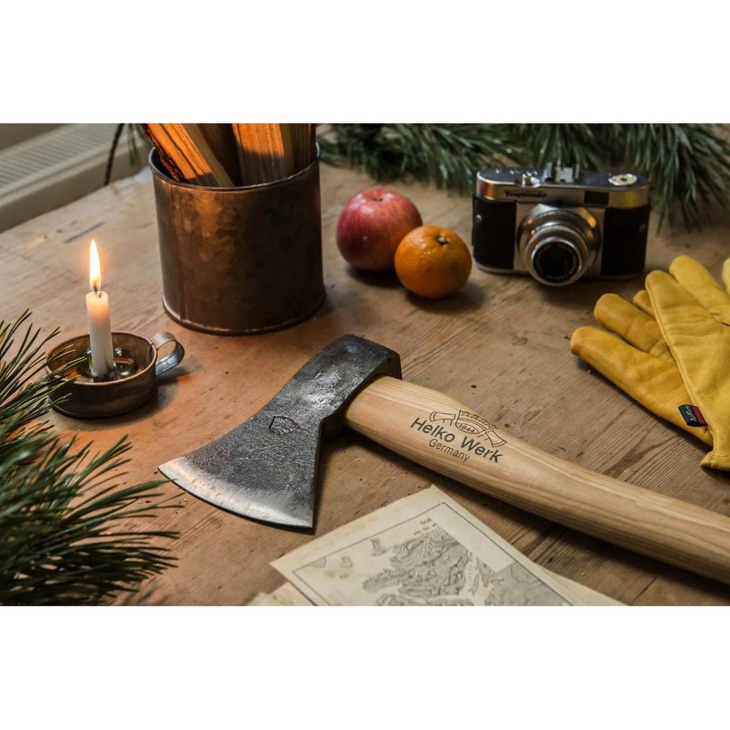 A close-up of the Helko Werk Rheinlander Hatchet on a wooden table with a camera, apples, and yellow gloves in the background.