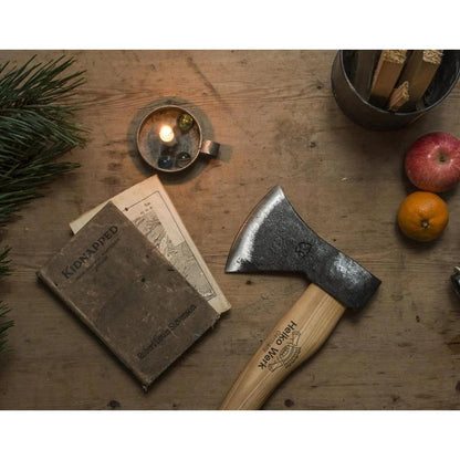 A wooden table with a Helko Werk Rheinlander Hatchet, a book, a lit candle, and a red apple.
