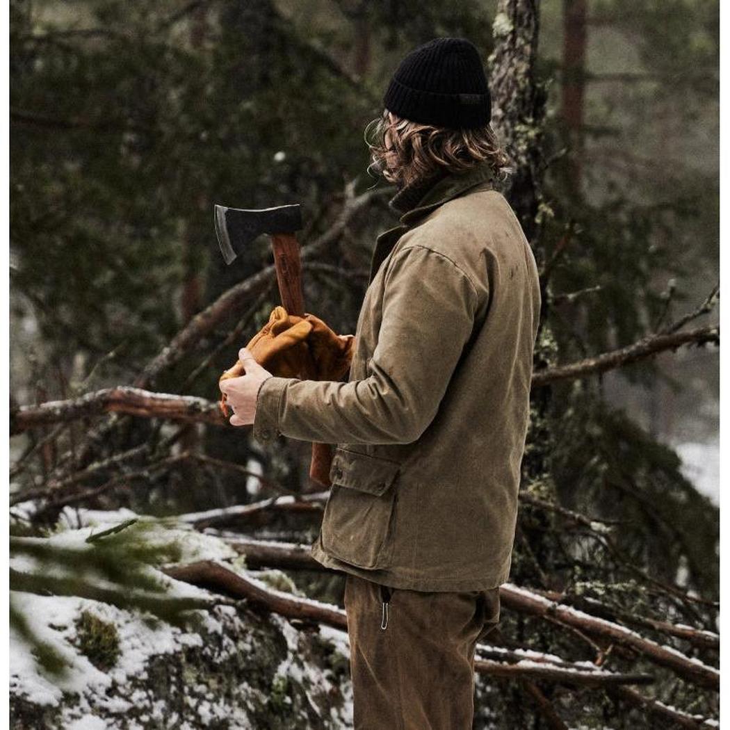 A person in a brown jacket and black beanie holds the Helko Werk Rheinlander Pack Axe in a snowy forest setting.