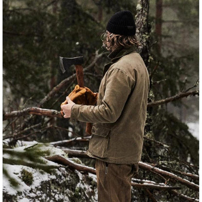 A person in a brown jacket and black beanie holds the Helko Werk Rheinlander Pack Axe in a snowy forest setting.