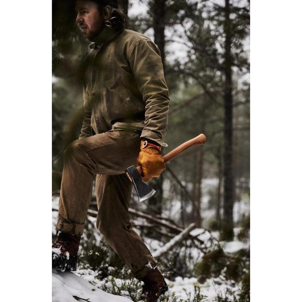 A man in brown workwear holds the Helko Werk Rheinlander Pack Axe while stepping on snow in a forest.