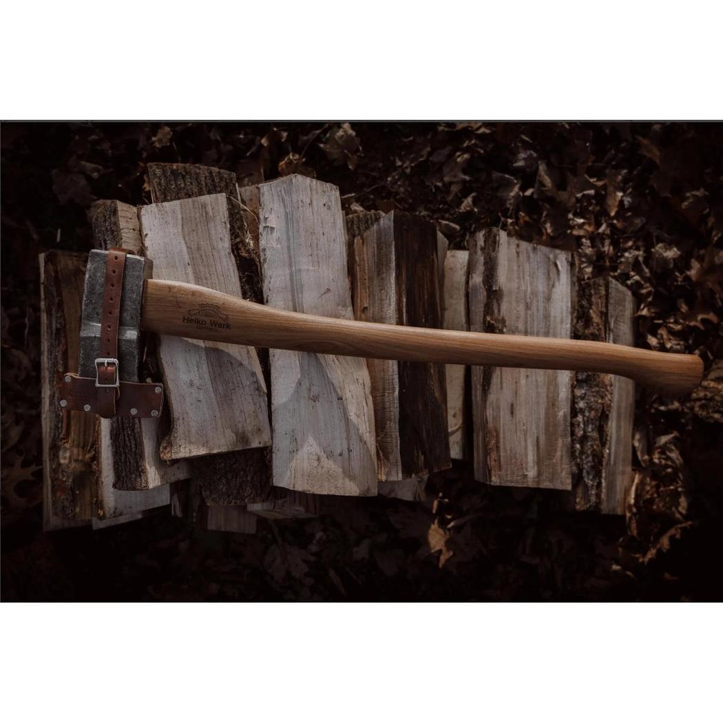 A Helko Werk Saxon Splitter axe rests on a stack of split firewood with a dark leafy background.