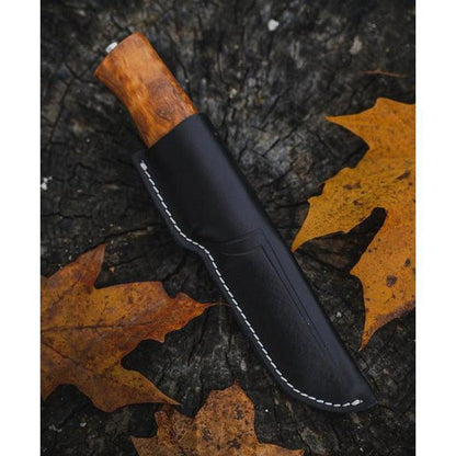 A side view of the Helle Eggen 12C27 knife with a wooden handle in a black sheath, resting on a tree stump with autumn leaves.