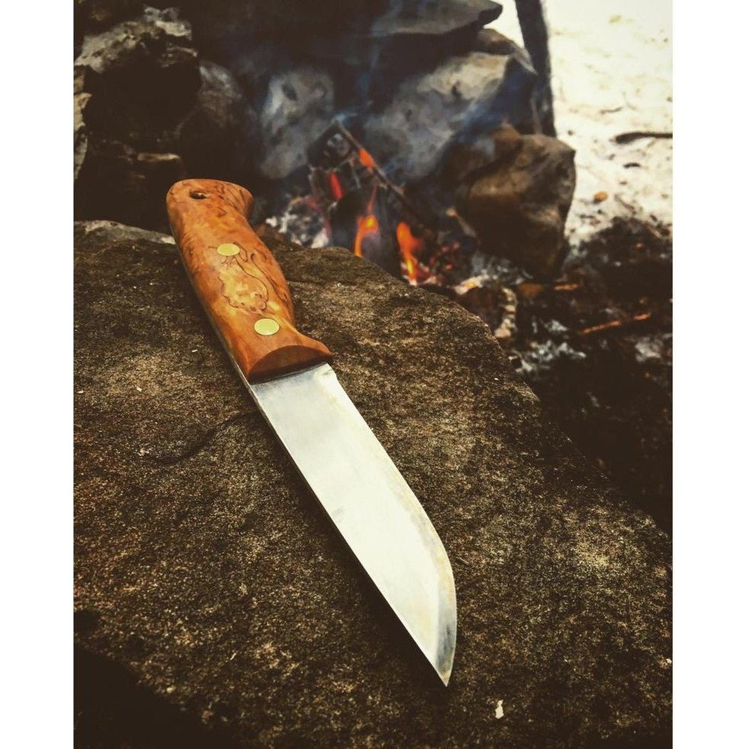 A Helle Temagami Laminated knife rests on a rock with a campfire burning in the background.