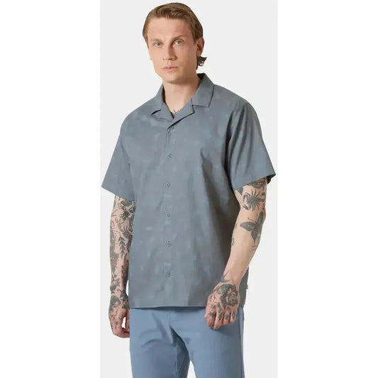A front view of the Helly Hansen Men's Holmen Short Sleeve Shirt in Washed Navy/Pine Needle on a model with tattoos against a plain background.