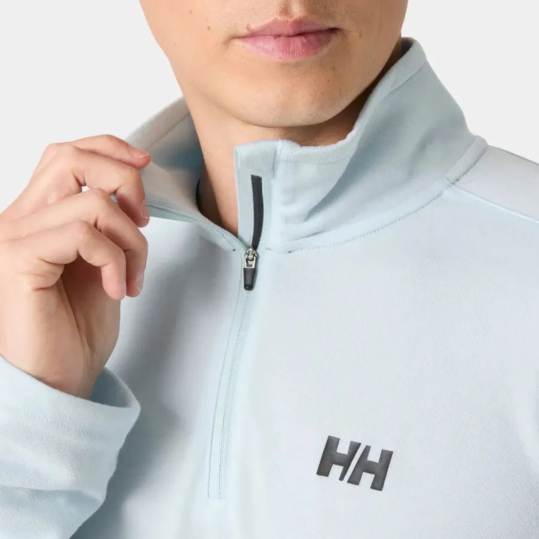 A close-up of a man wearing the Helly Hansen Men's HP Half-Zip Pullover 2.0 in Barely Blue, showing the half-zip and logo on a light background.
