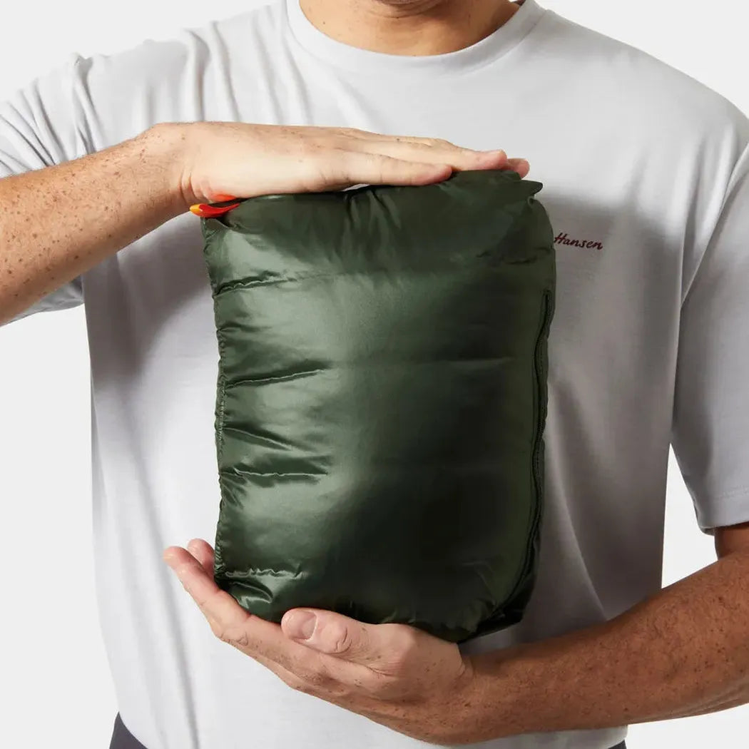 A man holds the Helly Hansen Men's Verglas Hooded Down Jacket 2.0 in Jungle Green, showing the compacted jacket against a white background.