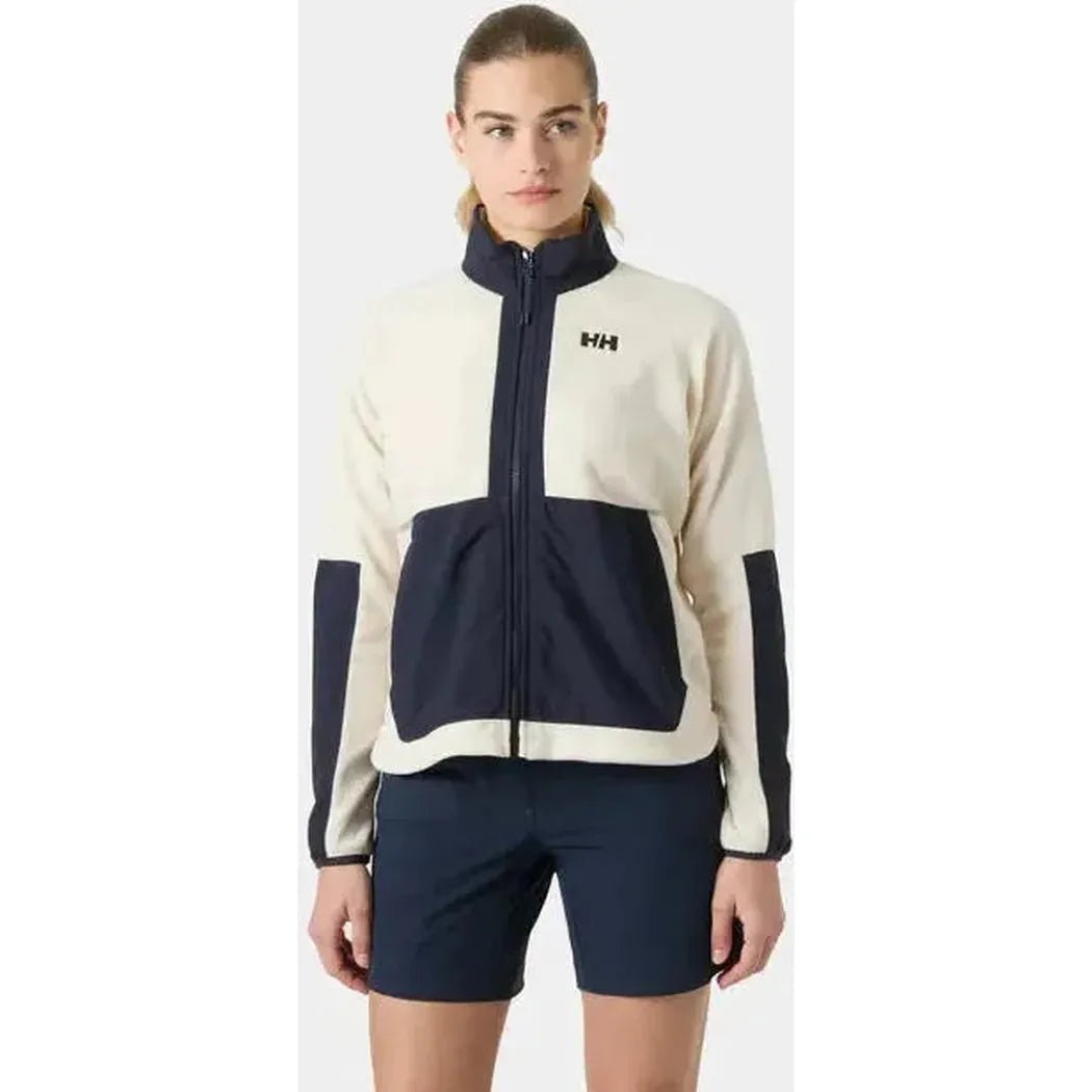 A front view of the Helly Hansen Women’s Rig Fleece Jacket in Cream with a dark blue pocket and sleeve accents on a model wearing dark shorts against a plain background.