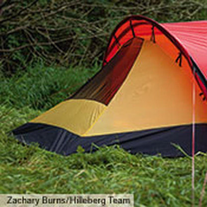 A side view of the Hilleberg Anjan 3 GT Sand tent in a grassy outdoor setting with trees in the background.