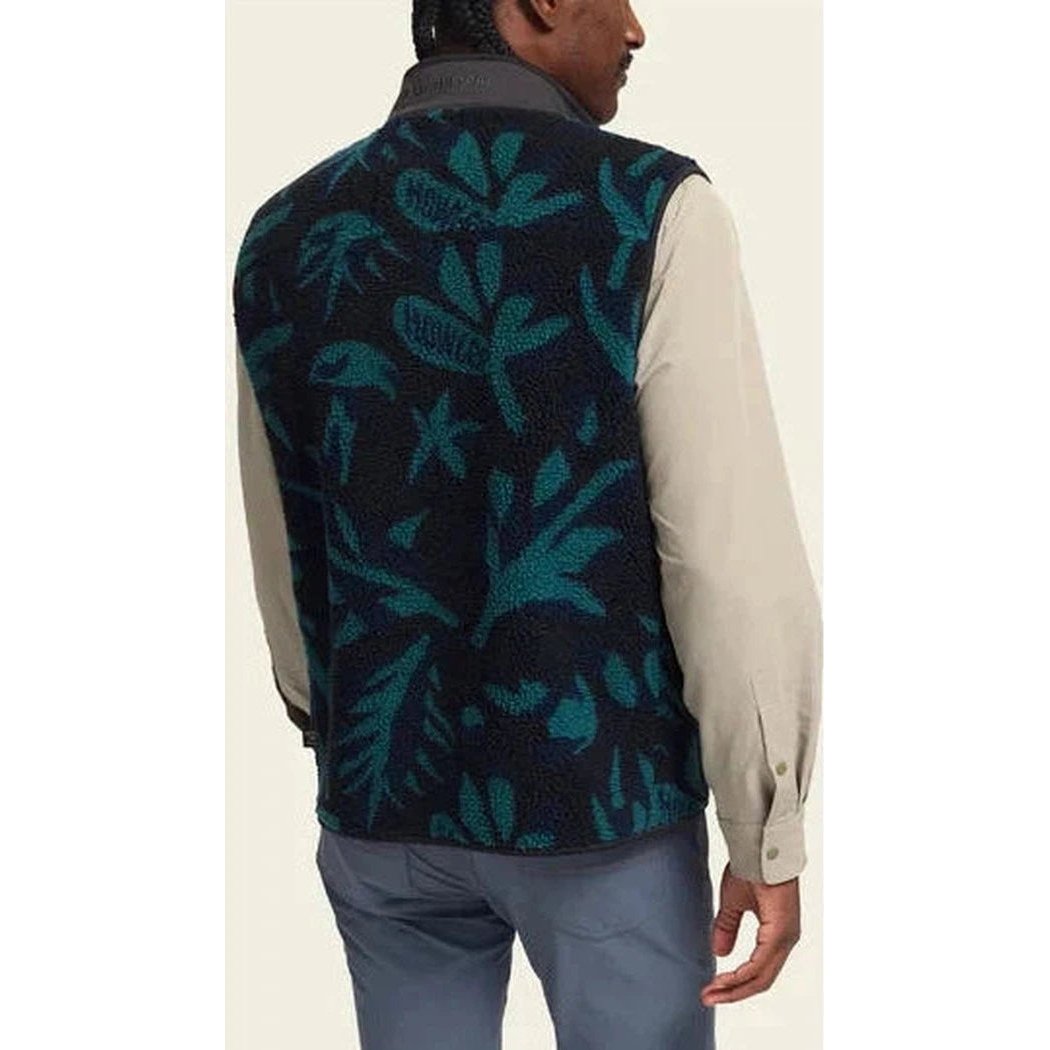 Back view of the Howler Brothers Men's Chisos Fleece Vest in Antique Black with a leaf pattern, worn by a man in blue pants against a plain background.