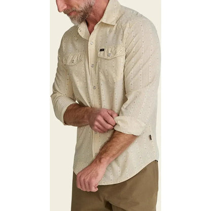 A man wearing the Howler Brothers Men's H Bar B Tech Longsleeve in Supernova Stripe : Leche rolls his sleeve up, shown from the side against a plain background.