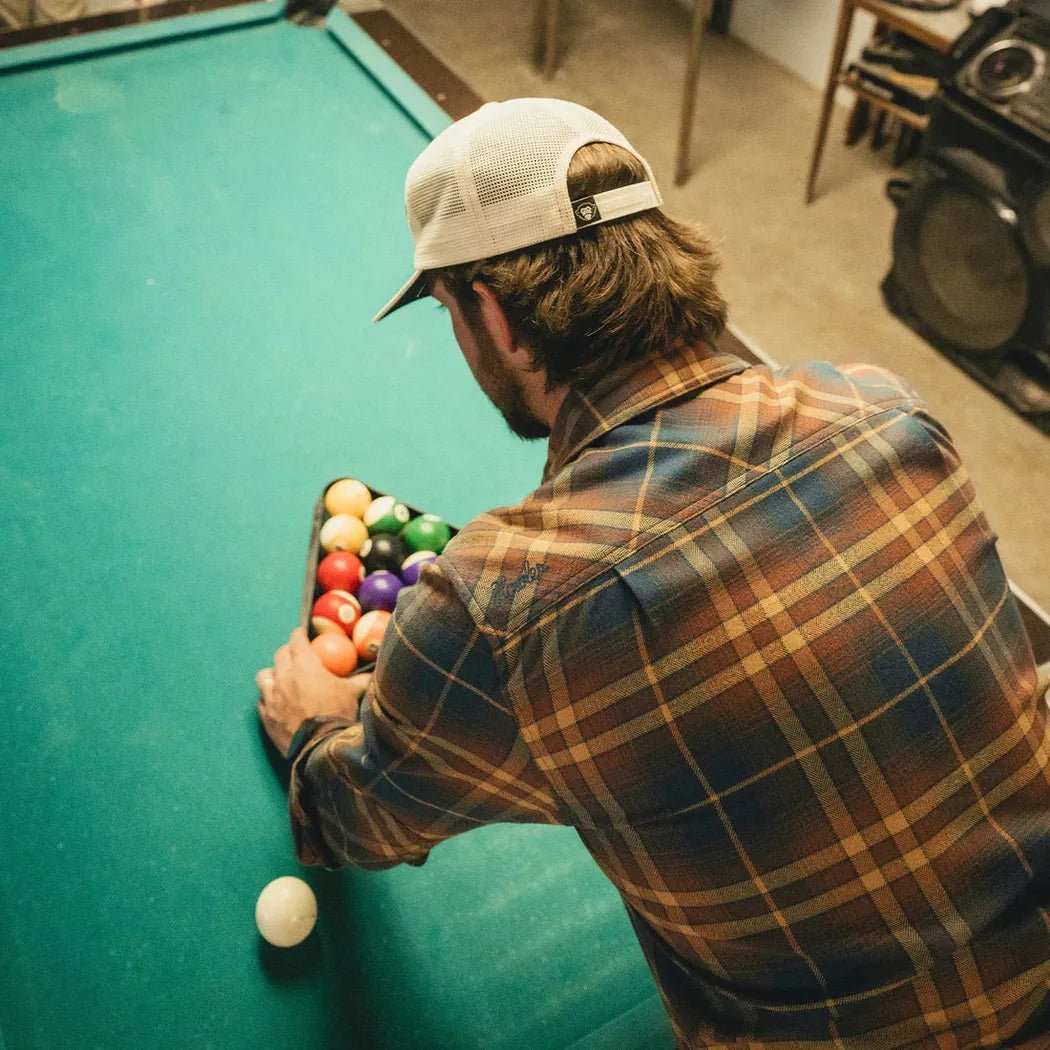 A man in a Howler Brothers Men's Harker Flannel Kempton Plaid : Stargazer shirt prepares to play pool, showing the plaid pattern and casual fit.