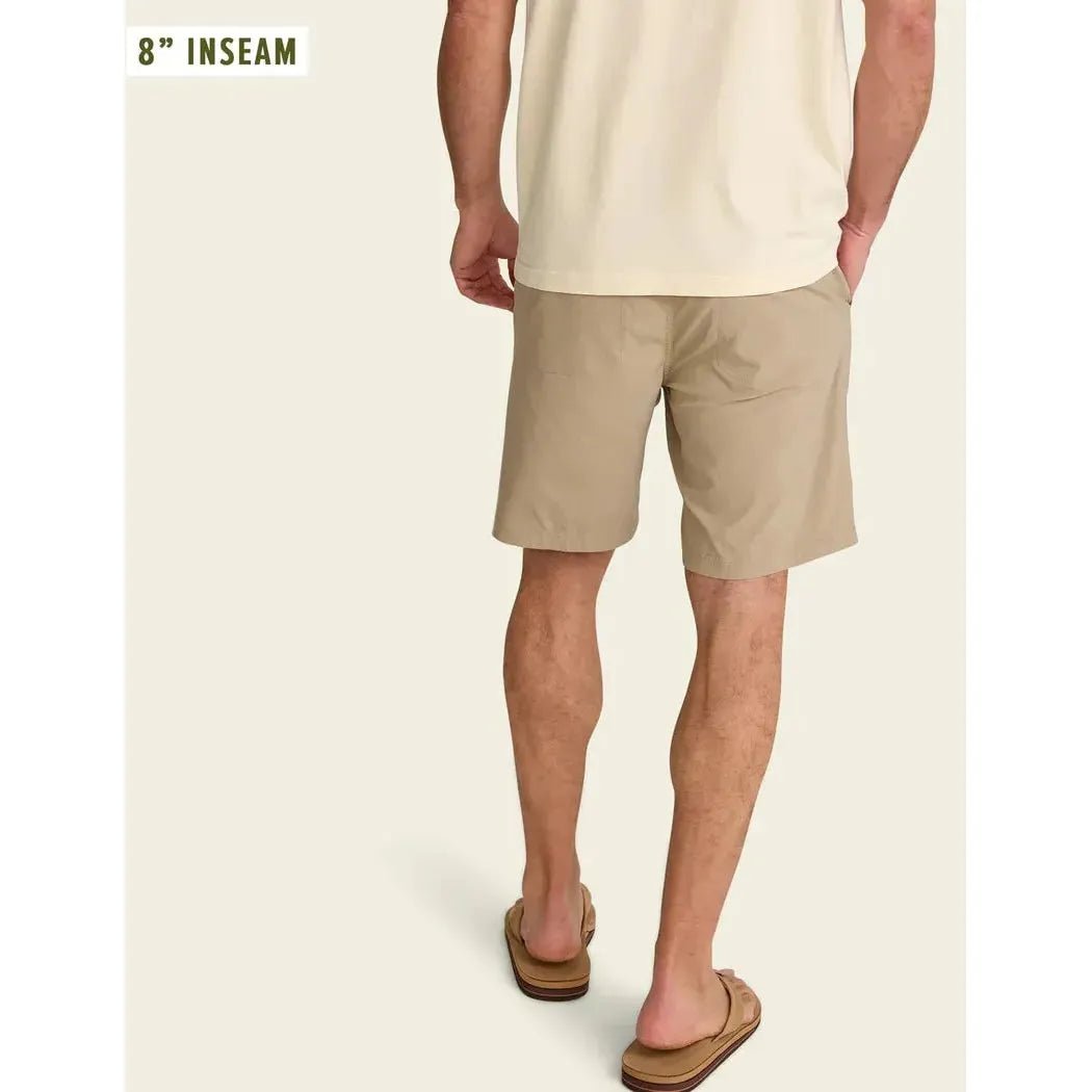 Back view of Howler Brothers Men's Horizon Tech Shorts - 8" in Driftwood, model wearing them with flip flops against a plain background.