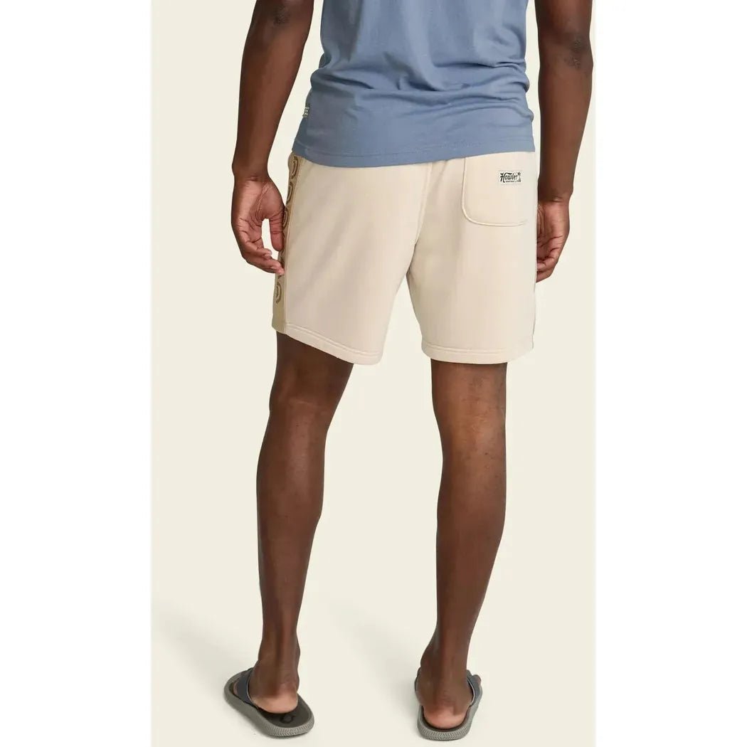 Back view of the Howler Brothers Men's Palmetto Chill Shorts in Oatmeal Heather on a model wearing gray flip flops against a plain background.