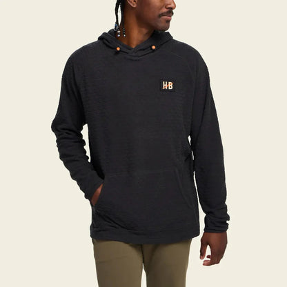 A man wearing the Howler Brothers Men's Palo Duro Fleece Hoodie in Antique Black stands against a plain background.