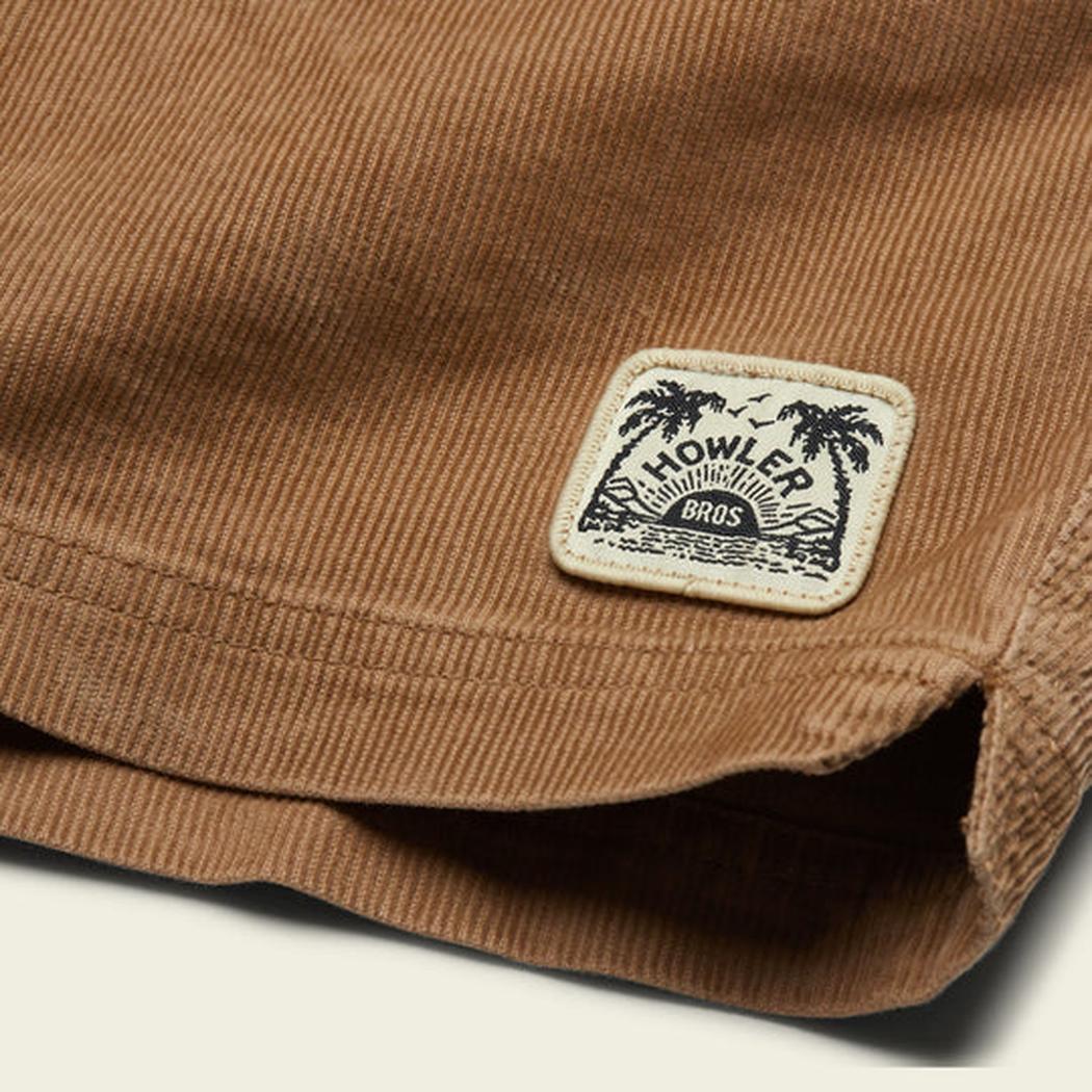A close-up of the Howler Brothers Men's Pressure Drop Cord Shorts in Lichen Green showing the brand patch on the pocket.