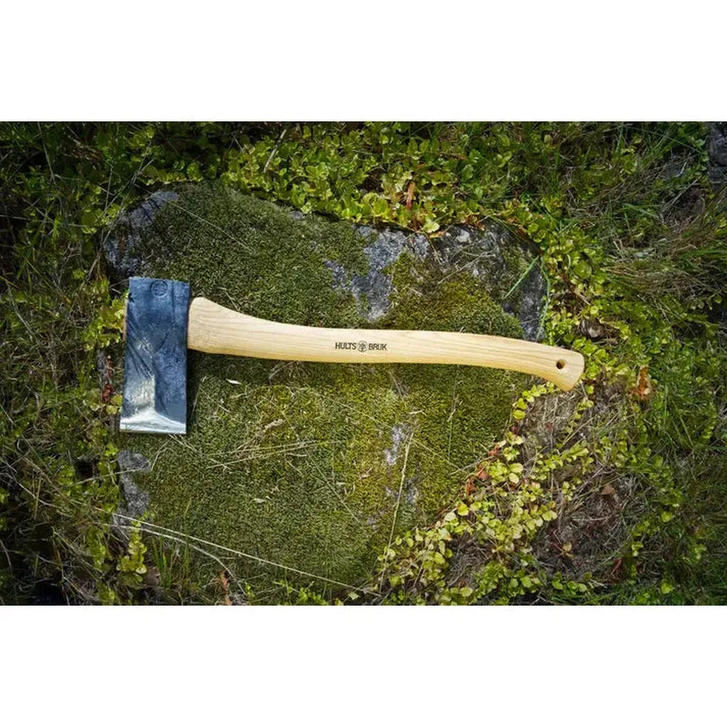 A natural wood handled Hults Bruk Jakobsdal Splitting Axe rests on a mossy rock in a grassy outdoor setting.