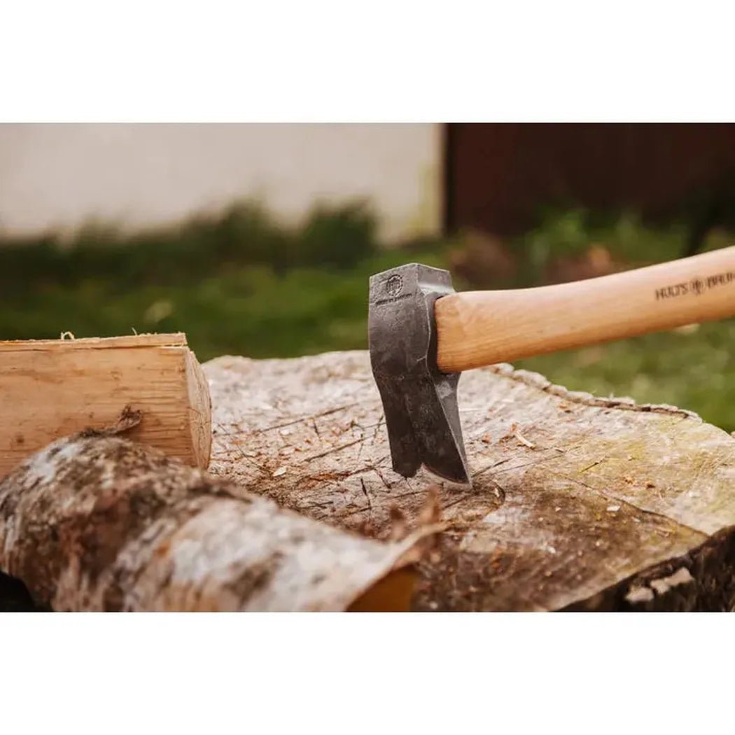 A Hults Bruk Kvillinge Splitting Axe rests on a split log with a piece of wood nearby, set against a blurred outdoor background.