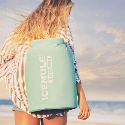 A woman on the beach carries a large Crimson Red IceMule Cooler Classic 20L.