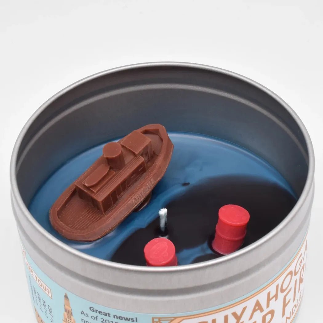A tin of the JD and Kate Industries Cuyahoga River Fire Scented Candle shows a brown boat model on blue wax with two red candles inside.