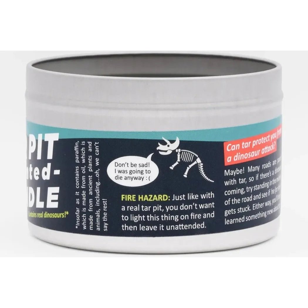 A close up of the JD and Kate Industries Tar Pit Scented Candle in a silver metal tin with a black label showing a dinosaur graphic and fire hazard warning.