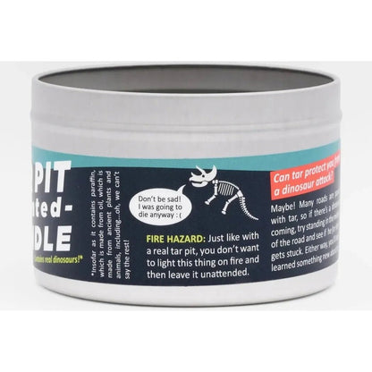 A close up of the JD and Kate Industries Tar Pit Scented Candle in a silver metal tin with a black label showing a dinosaur graphic and fire hazard warning.