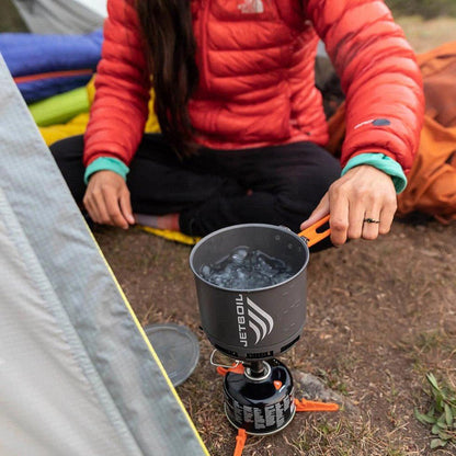 A woman in a red jacket cooks with a JetBoil Stash Cooking System on a campsite.