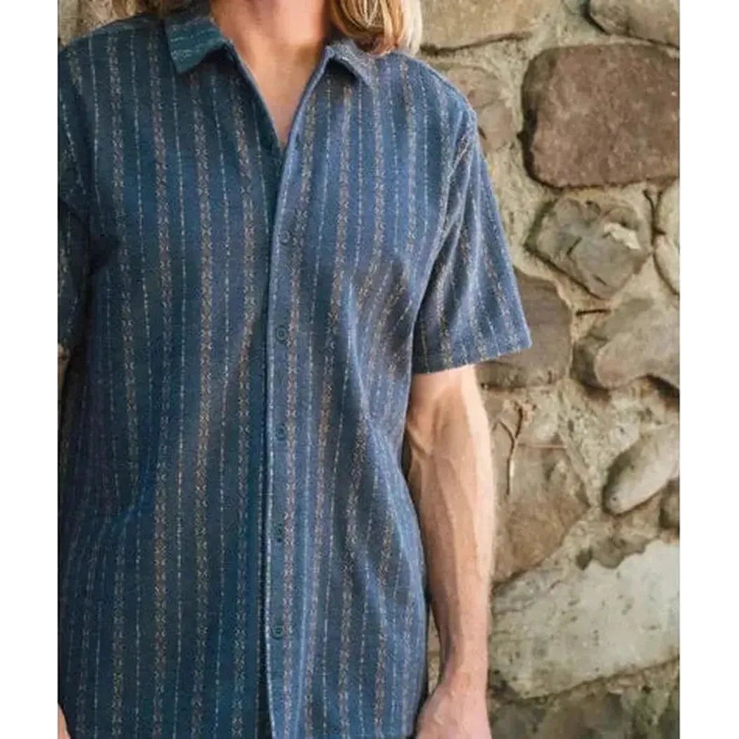 A front view of the Jetty Men's Asbury Knit Button Down in Navy, showing the short sleeves and button front against a stone wall background.