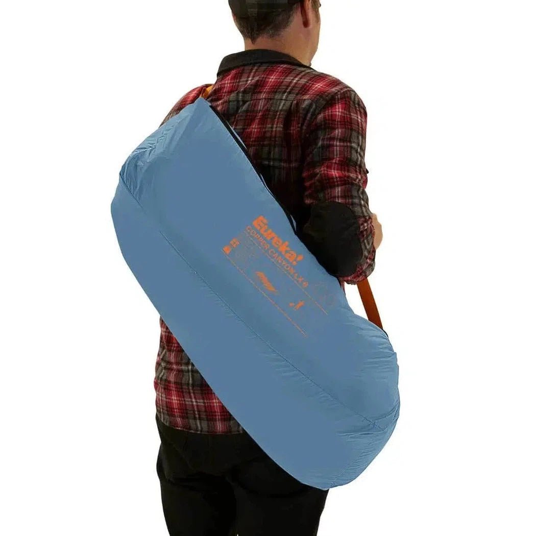 Back view of the Johnson Outdoors Eureka! Copper Canyon LX 6 tent in blue, carried by a model against a white background.