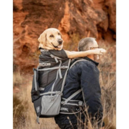 A man wears the Black K9 Sport Sack Rover 2 with a yellow lab in the pack, set against a rocky outdoor background.