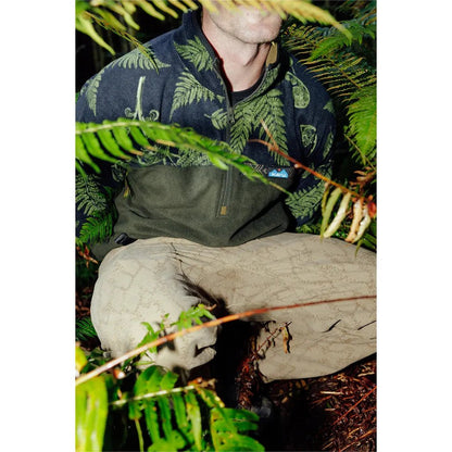 A man wearing the Kavu Men's Winter Throwshirt in Fiddlehead sits among ferns and foliage.