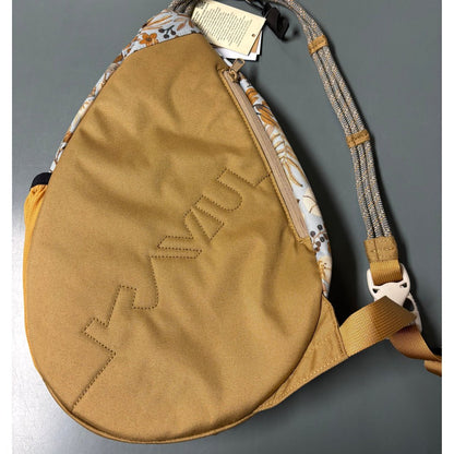 A top-down view of the Kavu Mini Paxton Pack in Forest Pass with a floral pattern on the back panel and a tan front pocket, against a gray background.