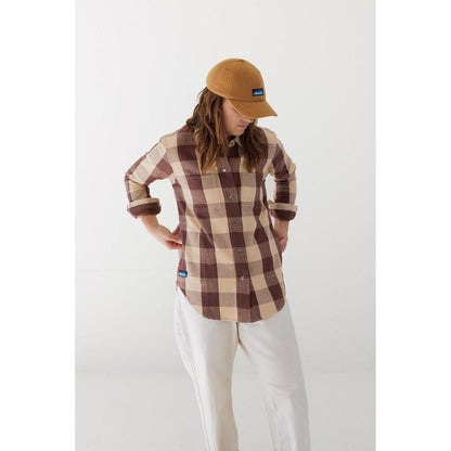 A model wears the Kavu Toasty Topper Blackout hat with a plaid shirt and white pants against a white background.