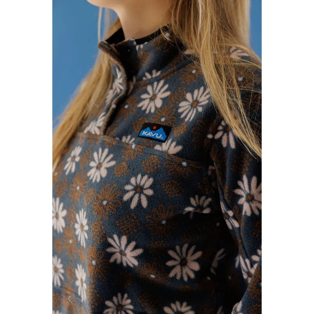 A close-up of the Kavu Women's Cavanaugh Fall Floral top on a model, showing the front pocket and logo against a blue background.