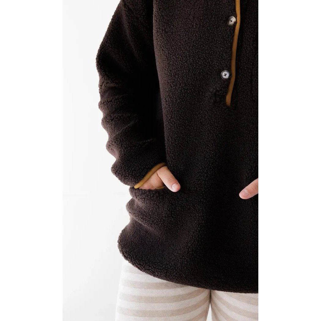 A close-up of the Kavu Women's Roselake Coffee top with a model's hands in the pockets against a white background.