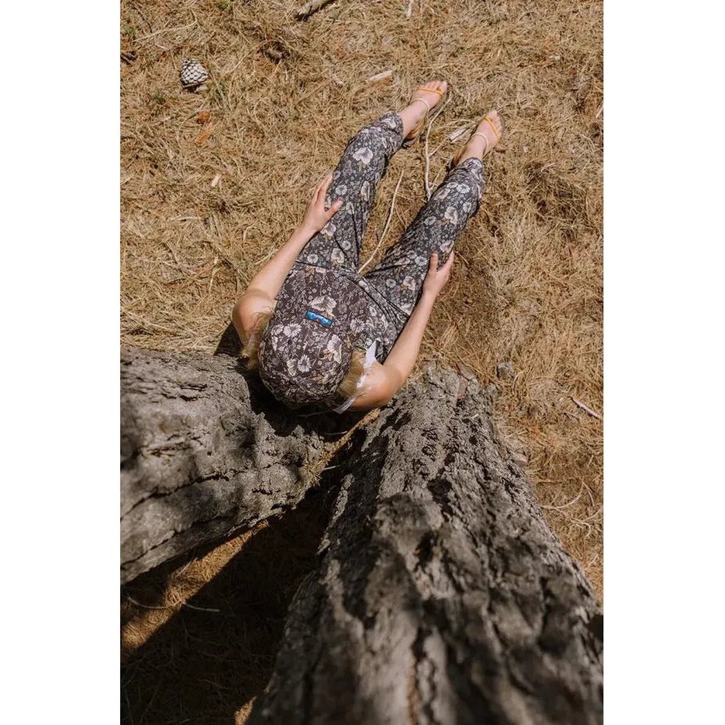A woman wearing Kavu Women's San Blas in Daisy Love lies on dry grass next to a tree trunk.