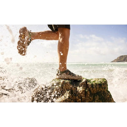 A man steps on a rock in the ocean wearing the Keen Men's Hyperport H2 in Martini Olive/Plaza Taupe.