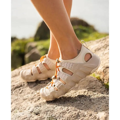 A woman’s feet in a side view of the Keen Women’s Hyperport H2 sandals in Birch/Plaza Taupe on a rocky outdoor surface.