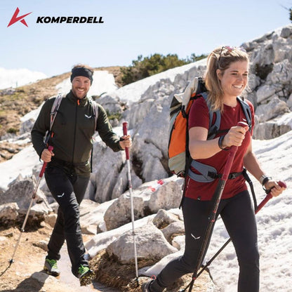 A man and woman hike with Komperdell Carbon PRO ZERO Compact trekking poles on a rocky, snowy trail.