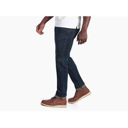Side view of the Kuhl Men's Kuhl Denim in Midnight showing the rolled cuffs and brown boots against a white background.