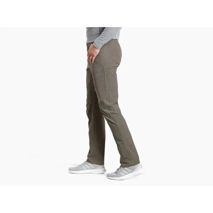 Side view of the Kuhl Men's Silencr Pant in Storm Khaki on a model wearing light gray sneakers against a white background.
