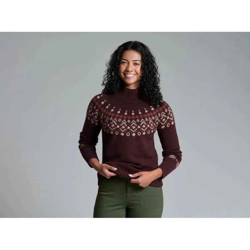 A woman wearing the Kuhl Women's Alpina Sweater in Alpine White stands against a gray background.