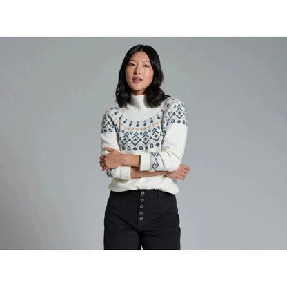 A model wearing the Kuhl Women's Alpina Sweater in Alpine White stands with crossed arms against a gray background.